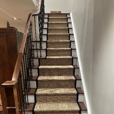Staircase with natural sisal runner, black border, and dark wood railing.